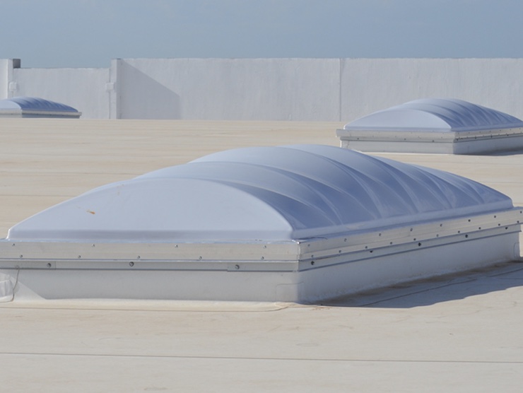 Curb-mounted acrylic dome skylights across a white commercial roof
